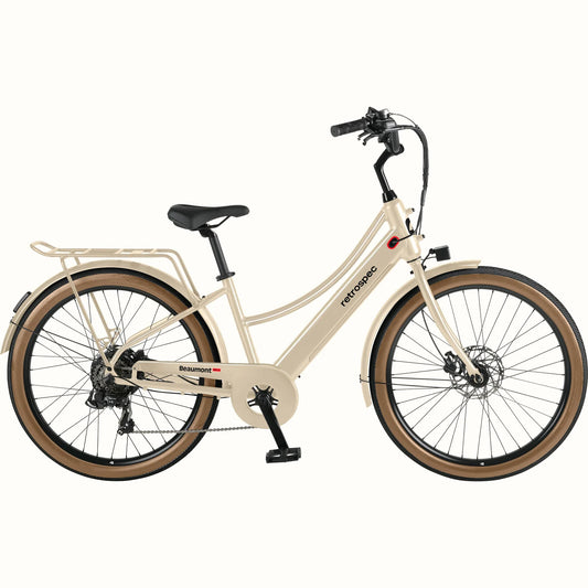 Retrospec Beaumont Rev 3 Plus electric bike in oat color, side view, featuring step-through frame, rear rack, and brown saddle and grips.