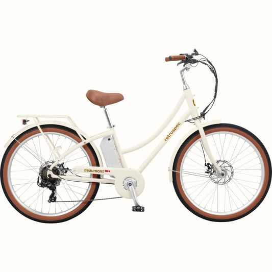Retrospec Beaumont Rev 3 electric bike in eggshell color, side view, featuring step-through frame, rear rack, and brown saddle and grips.